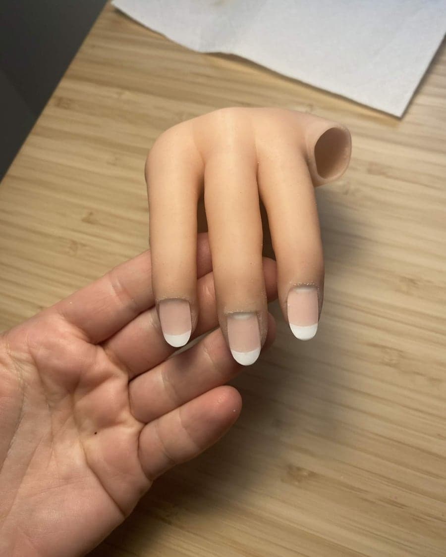 A lifelike 3D printed partial prosthetic hand resting across an open human hand.