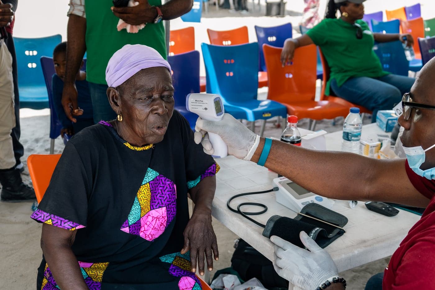 An older woman in a brightly patterned top having her temperature taken with an infrared thermometer.