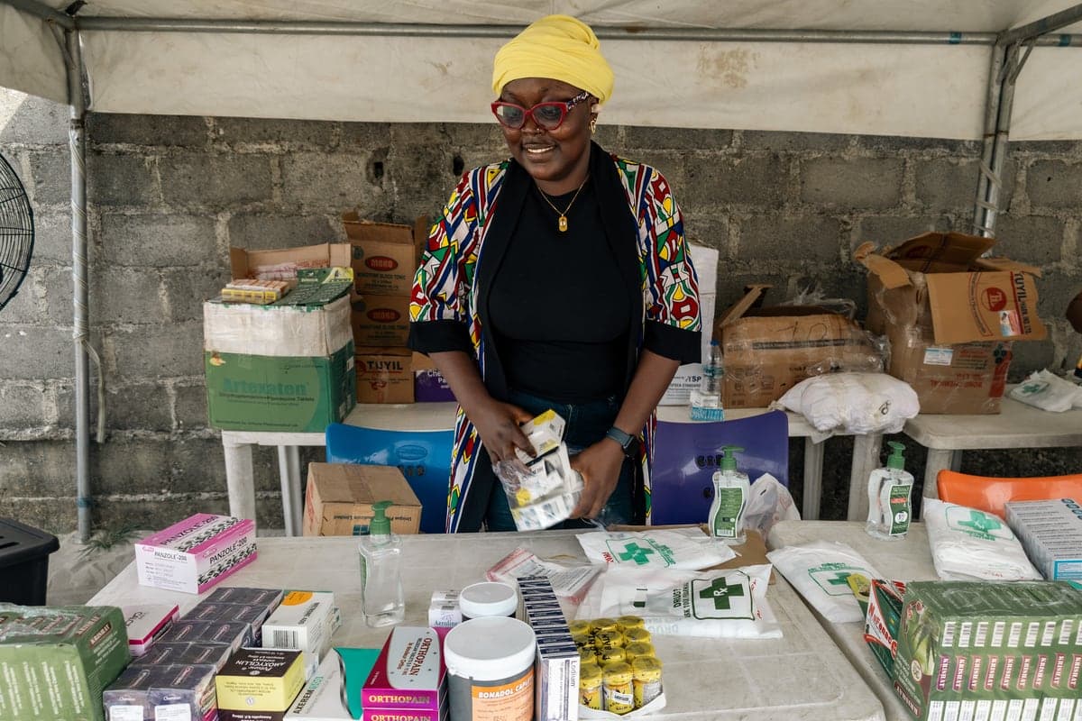 A volunteer pharmacist at a table stacked with boxed medicines.
