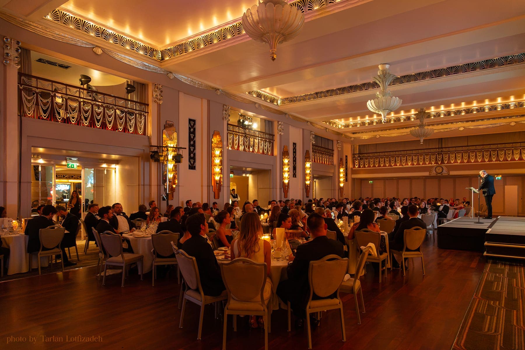 The ballroom at the Sforza Foundation's 2025 Inaugural Gala Ball, seen from the back: full tables under chandeliers and a speaker at the podium.