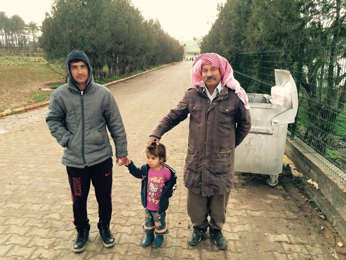 Three generations of a family standing together on a road at a Syrian refugee camp.